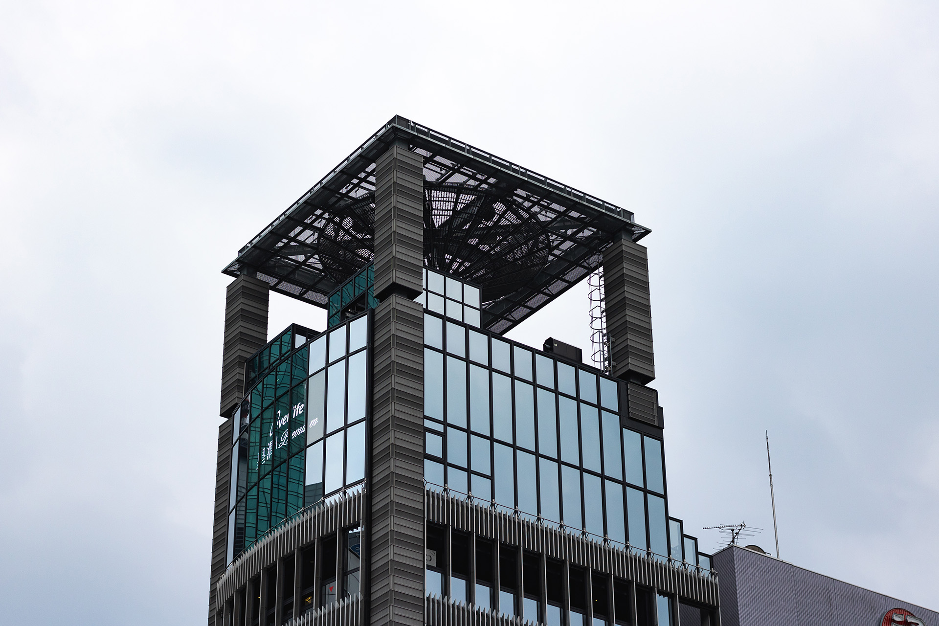 Rooftop terrace of a metallic building, the roof over it held up by a pillar in each corner, seen from below.